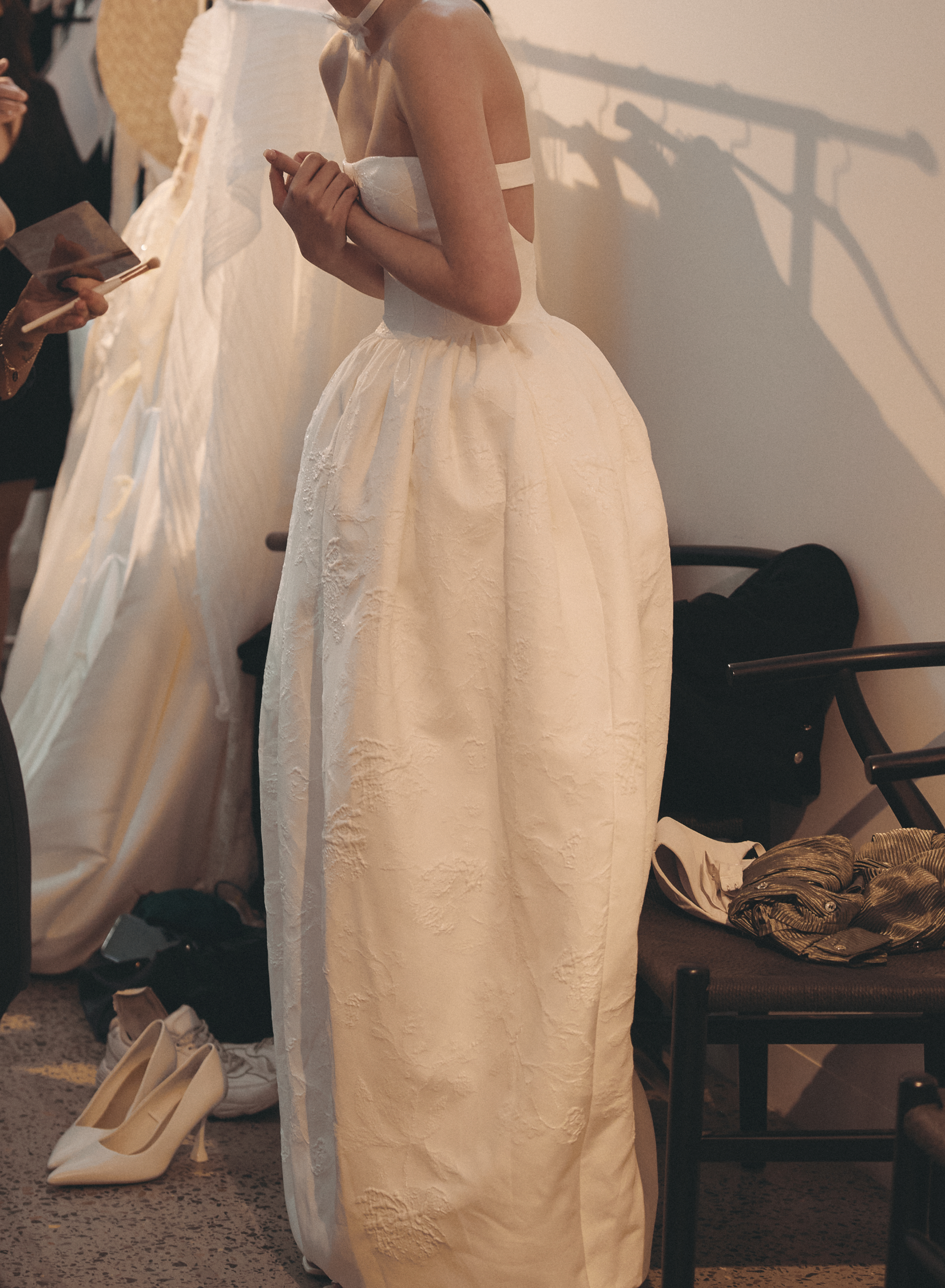 Woman wearing a white wedding dress in a room with other people and furniture.
