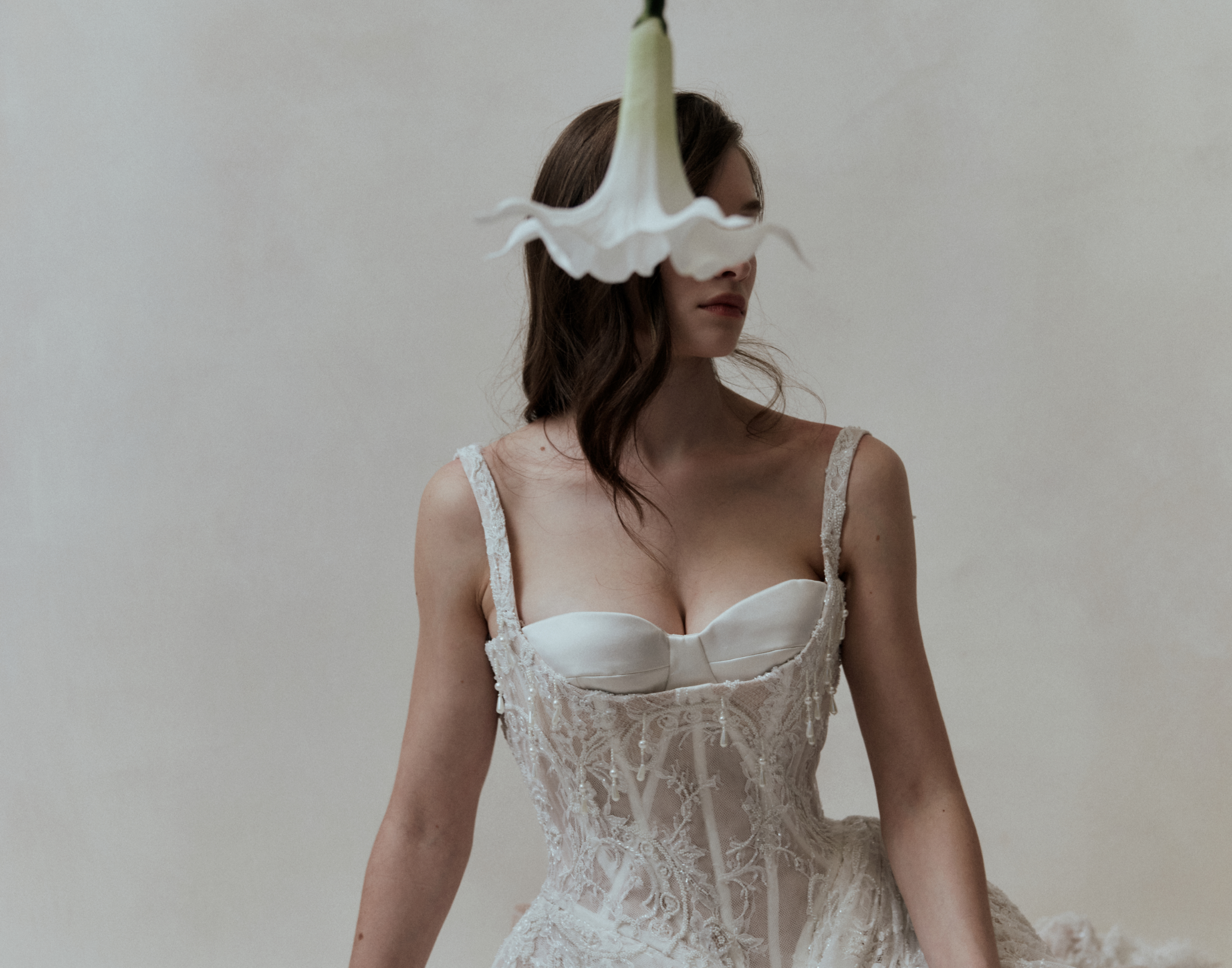 Woman wearing a white lace dress with a white flower covering her face against a plain background